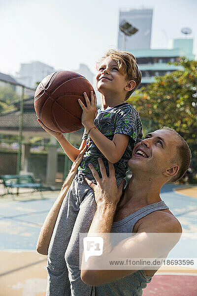 Glücklicher Vater mit Sohn  der an einem sonnigen Tag Basketball spielt