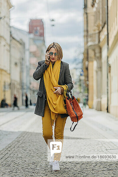 Stylish mature woman talking on mobile phone walking on city street