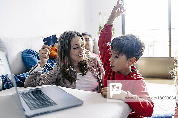 Mutter hält Kredit von Sohn mit erhobener Hand zu Hause am Laptop
