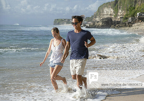 Glückliches junges Paar läuft am Strand im Meerwasser