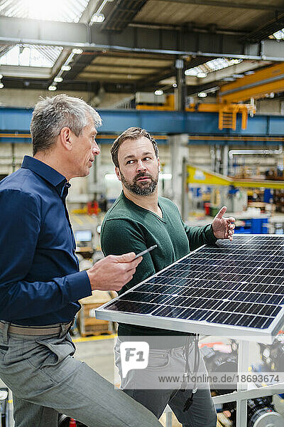 Mature manager discussing over solar panel with businessman at factory