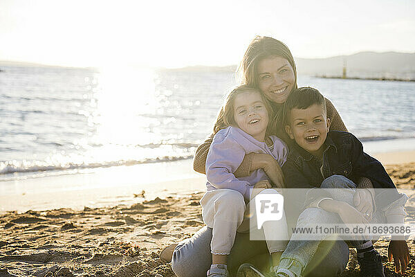 Smiling woman sitting with son and daughter at beach