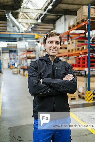Smiling employee with arms crossed standing in factory