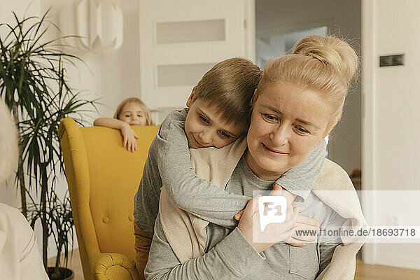 Junge umarmt Großmutter  die zu Hause sitzt