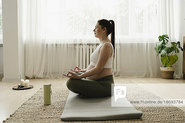 Pregnant woman meditating on exercise mat at home