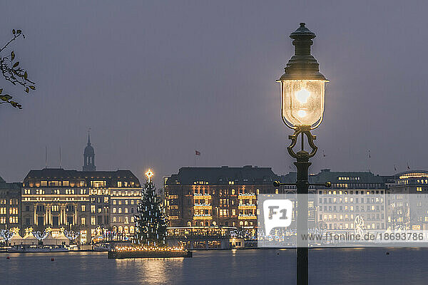 Germany  Hamburg  Street light glowing in front of Alster Lake at dusk with Christmas tree in background