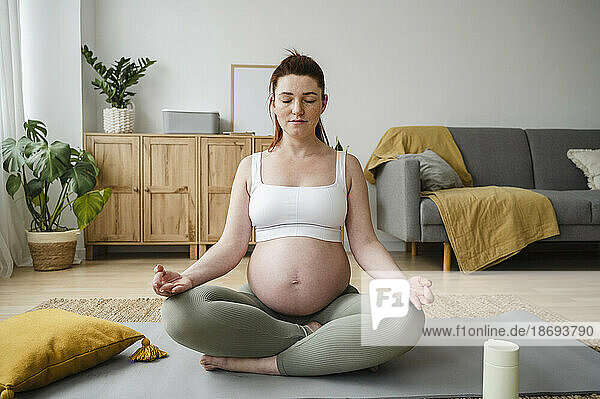 Pregnant woman with eyes closed meditating on exercise mat at home