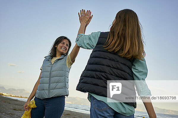 Happy activists giving high-five after cleaning beach