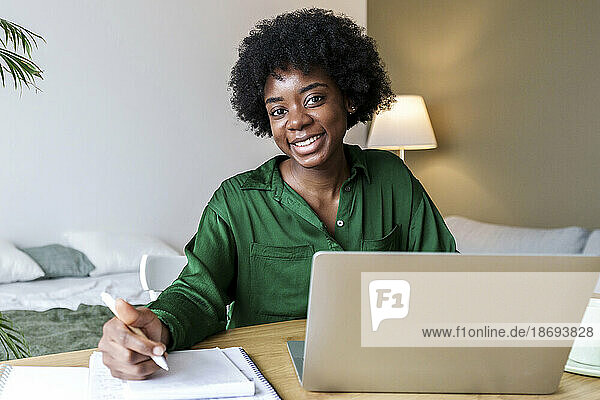 Happy businesswoman with pen and laptop sitting at desk