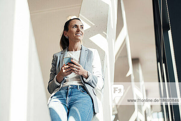 Thoughtful businesswoman with smart phone at office