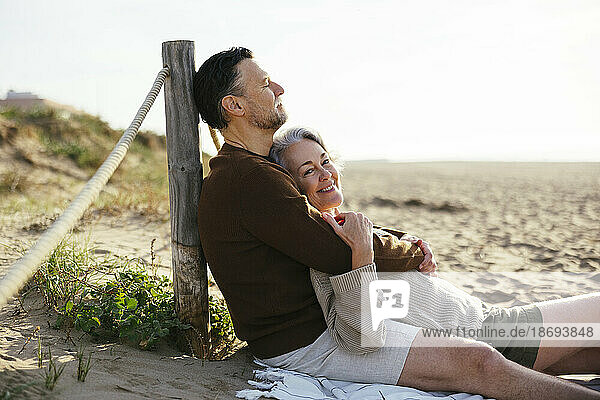 Mann umarmt Frau  die am Strand sitzt