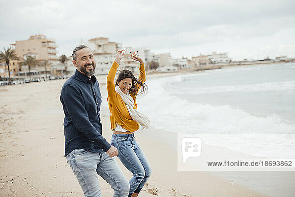 Cheerful man and woman dancing on coastline at beach