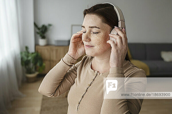 Pregnant woman with freckles adjusting headphones at home