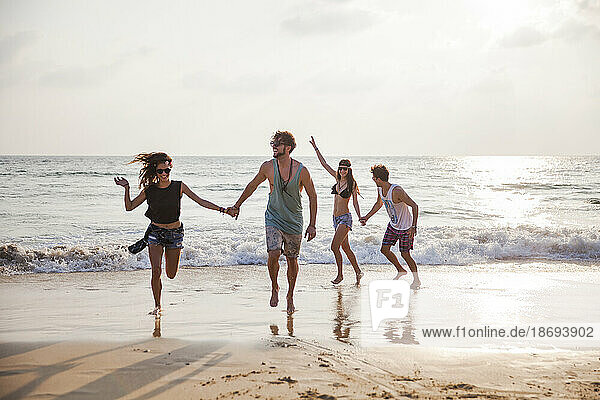 Fröhliche Freunde halten Händchen und spielen am Strand