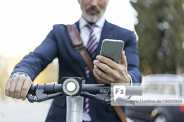 Businessman with electric scooter holding smart phone