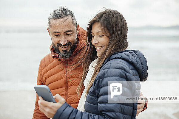 Glücklicher Mann und Frau  die am Strand ihr Smartphone benutzen