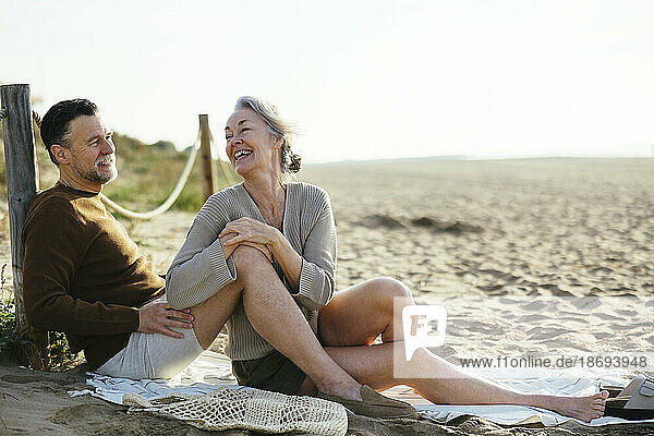 Happy woman talking to man sitting at beach