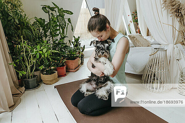 Woman kissing Schnauzer dog sitting on exercise mat at home