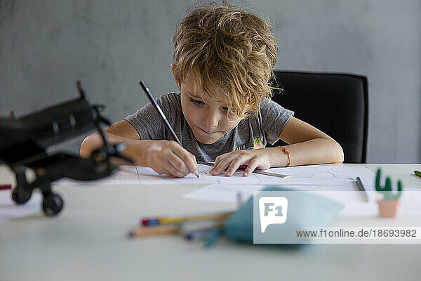 Junge schreibt mit Bleistift auf Papier am Schreibtisch