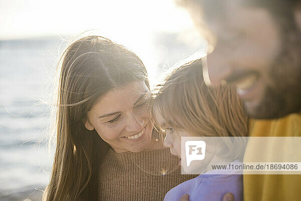 Lächelnde Frau mit Tochter am Strand an einem sonnigen Tag