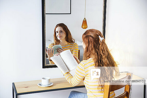 Redhead woman sitting with book in front of mirror