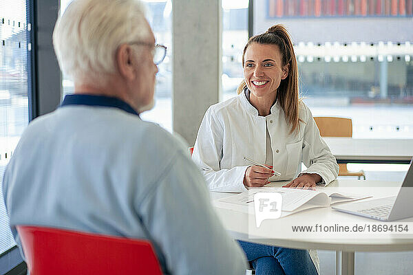 Happy doctor with file discussing with patient sitting at clinic