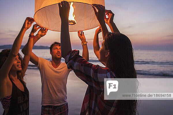 Woman holding lit paper lantern with friends at beach