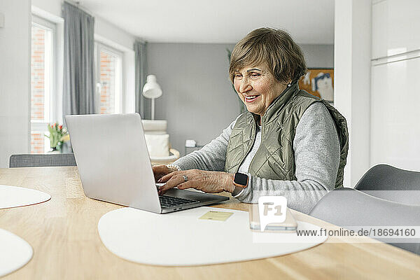 Lächelnde Frau  die zu Hause einen Laptop auf dem Tisch benutzt