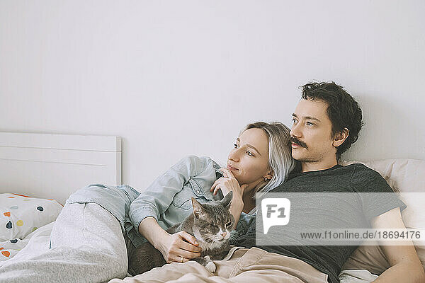 Thoughtful couple with cat lying on bed at home