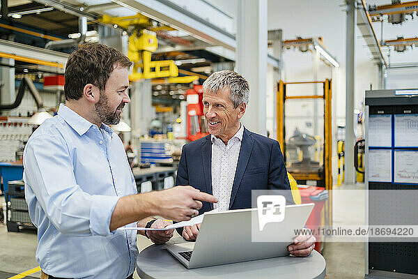 Manager pointing at laptop by businessman at factory