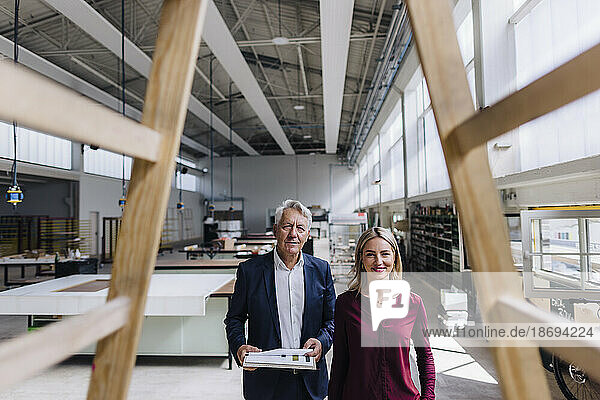 Lächelnde Geschäftsfrau und Geschäftsmann betrachten Holzkonstruktion in der Fabrik