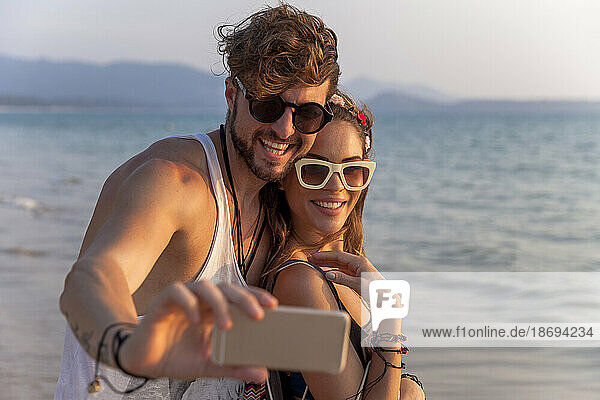 Man taking selfie through mobile phone with girlfriend at beach