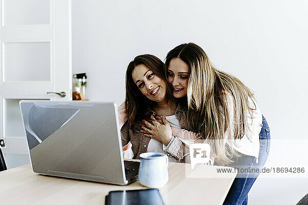 Daughter embracing mother using laptop at home