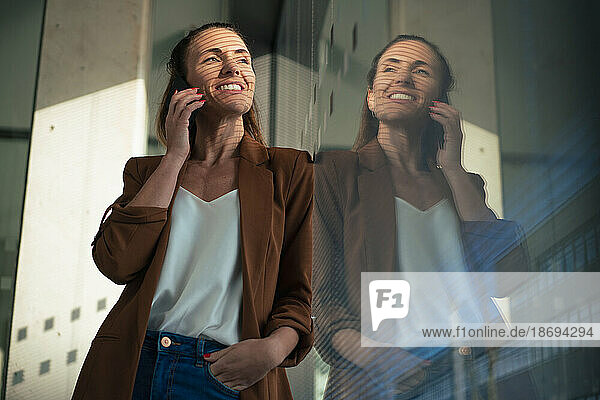 Smiling businesswoman talking on smart phone leaning at office