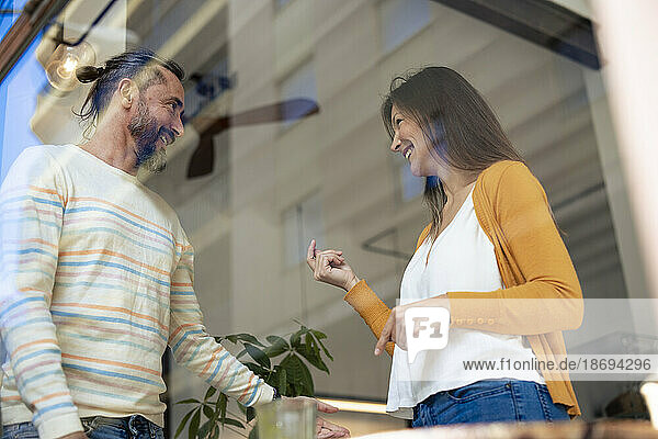 Glückliches Paar steht und redet im Café  gesehen durch die Glasscheibe