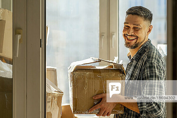 Lächelnder Mann hält Karton zu Hause
