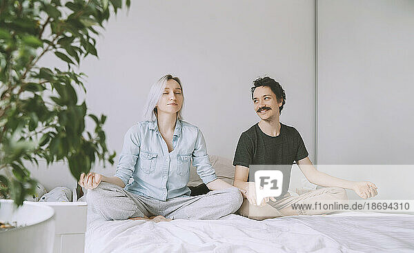 Smiling man and woman doing yoga on bed at home