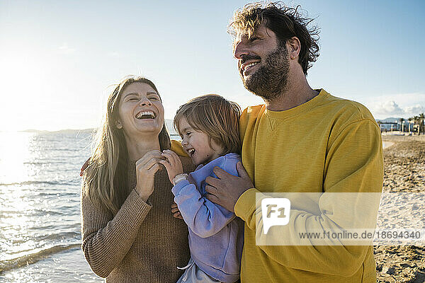 Frau lacht mit Tochter und Mann am Strand