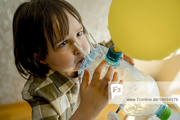 Boy blowing balloon through plastic bottle car at home