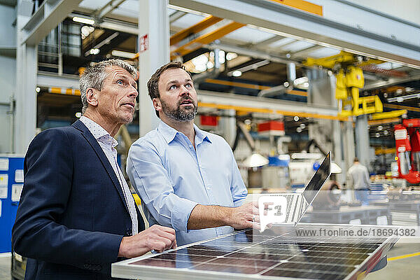 Manager and businessman looking up by solar panel at factory