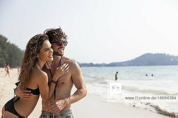 Lächelnde junge Frau umarmt ihren Freund am Strand