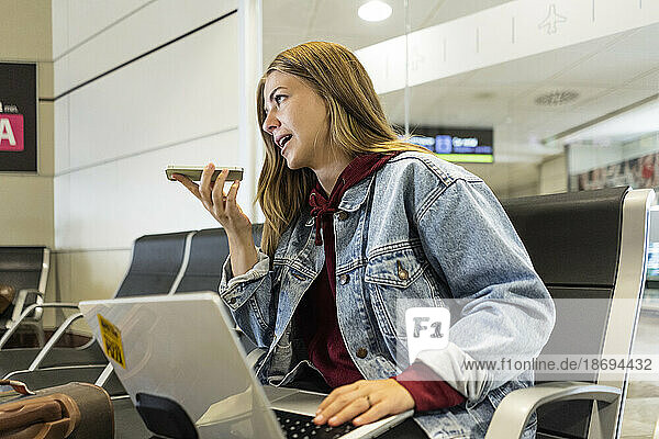 Young woman talking on speaker phone at airport lobby