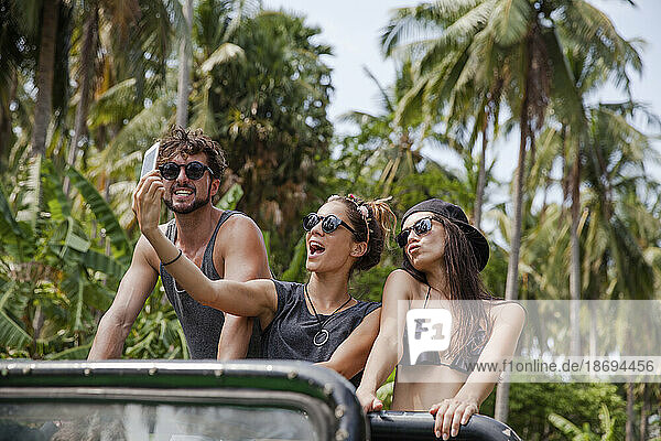 Friends taking selfie on off-road vehicle at beach