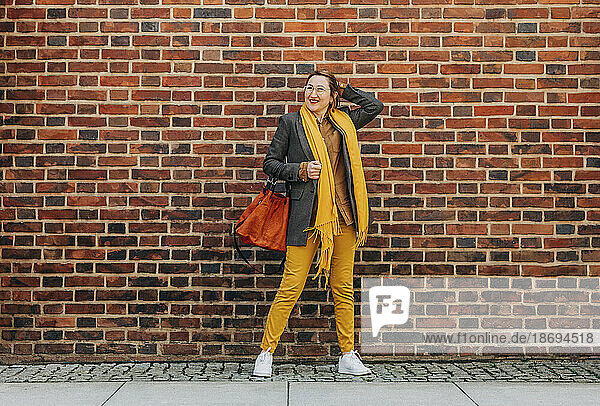 Stylish woman with scarf and jacket standing in front of brick wall
