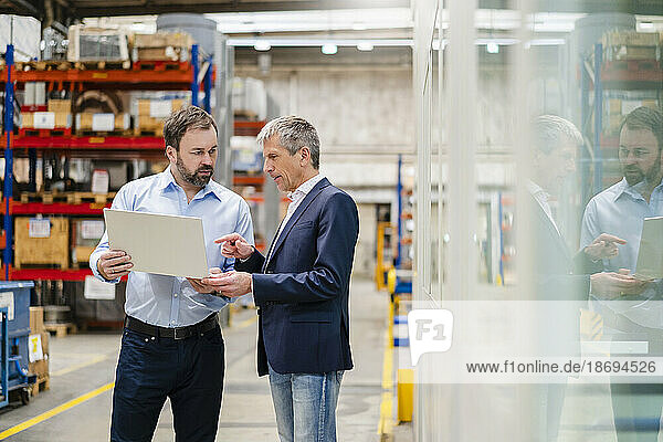Businessman discussing with manager over laptop at factory