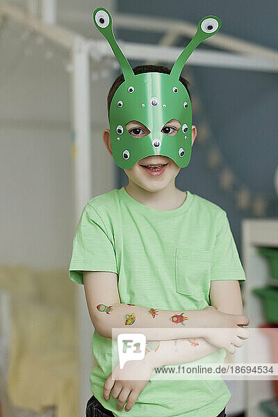 Boy with stickers on hand wearing green alien mask