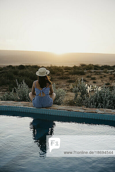 Woman looking at sunset sitting poolside