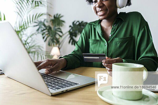 Happy woman using laptop and paying with credit card at office
