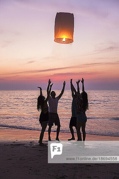 Friends releasing lit paper lantern standing at beach on sunset