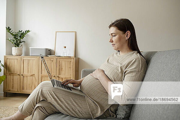Pregnant freelancer with hand on stomach working on laptop at home office